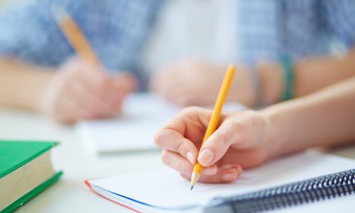 Hand of student with pencil carrying out written task or writing lecture